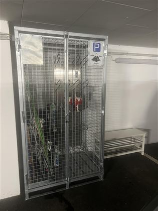 Een veilige fietsenstalling met hekken en een parkeerschild. Binnen zijn enkele fietsen en accessoires te zien.