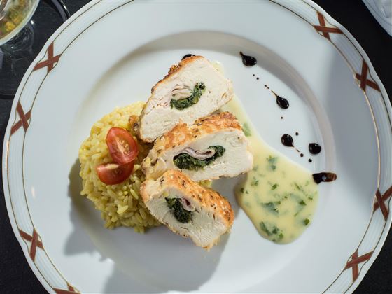 Ein leckeres Gericht mit gefülltem Hähnchenbrustfilet, serviert mit gelbem Reis und Kirschtomaten. Dazu gibt es eine cremige Sauce und ein geschmackvolles Püree.