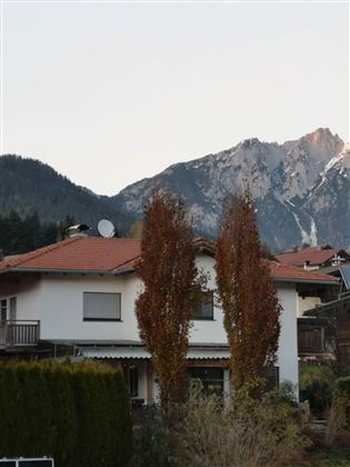 A cozy house with a red roof and a beautiful garden. Majestic mountains rise in the background.