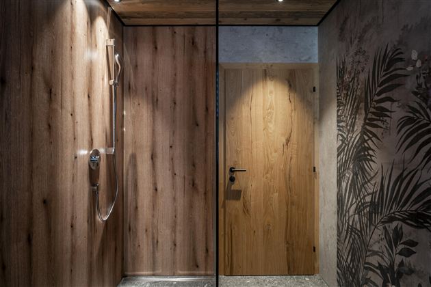 A modern shower with wood paneling and a glass partition. In the background, a door with a simple design is visible.