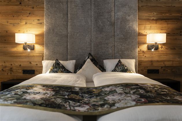 A stylish bedroom with two beds and a cozy wooden paneling. An elegant headboard and decorative pillows complete the ambiance.