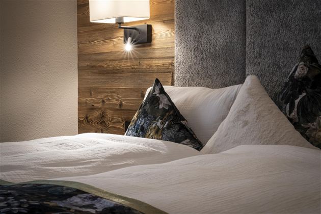 A cozy bedroom with a modern bed and decorative cushions. Soft light creates an inviting atmosphere.