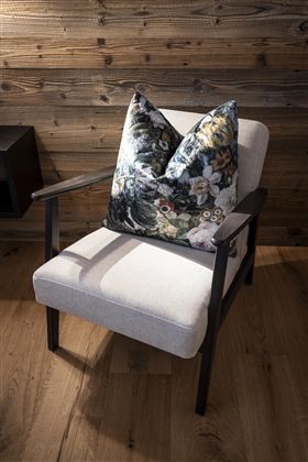 A comfortable armchair with a colorful cushion stands in front of a wooden wall. The room has a warm and inviting atmosphere.