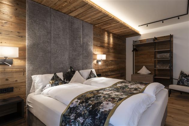 A modern bedroom with a large double bed and cozy wood paneling. The decorative pillows and soft lighting create an inviting atmosphere.