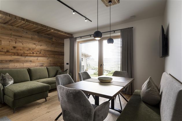 A stylish living room with a green couch and a modern dining table.  
Large windows let in plenty of light and provide a view outside.