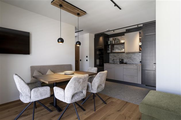 A modern dining room with a wooden table and comfortable chairs. In the background, a stylish kitchen is visible.