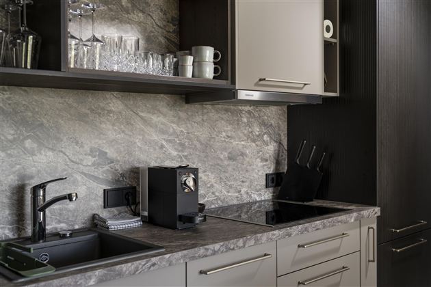 A modern kitchen with an elegant countertop and minimalist furniture. There are glasses, mugs, and a coffee machine on the countertop.