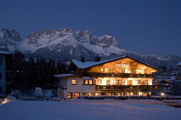 Ein schönes, beleuchtetes Gebäude im Schnee bei Nacht. Im Hintergrund erheben sich majestätische Berge.