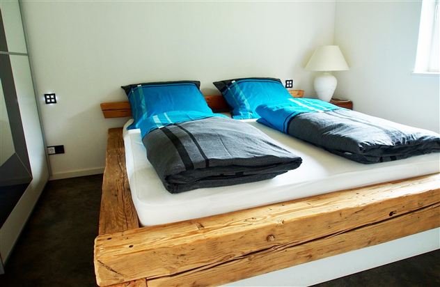 A cozy bedroom with two single beds and modern blue pillows. The floor is gray and there is a lamp next to the bed.