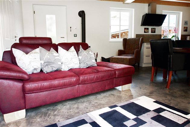A cozy living room with a red sofa and decorative cushions. In the background, there is a dining table and a television.