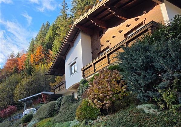 Een charmant huis te midden van een bosrijk landschap. Kleurige herfstbladeren en verzorgde struiken omringen het tafereel.