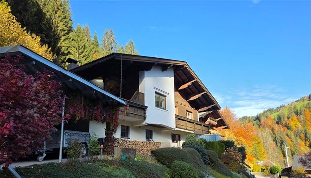 Een charmant huis met een groot balkon, omringd door kleurrijke bomen in de herfst. De heldere blauwe lucht vormt een verdere mooie tegenstelling.