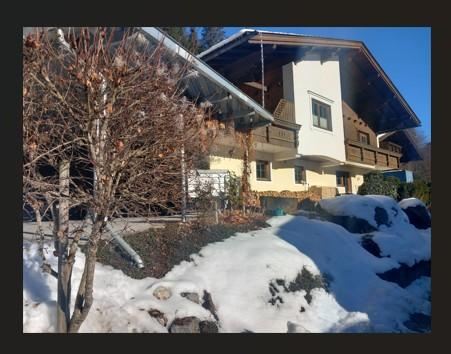 Een gezellig huis in de sneeuw met een heldere blauwe lucht. Omgeven door bomen en rotsen is het winterlandschap goed zichtbaar.
