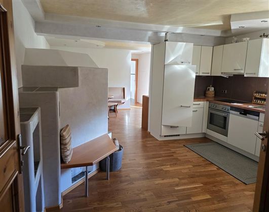 Een moderne keuken met lichte meubels en een open woonruimte. De vloer is van hout en er is een gezellige zithoek.