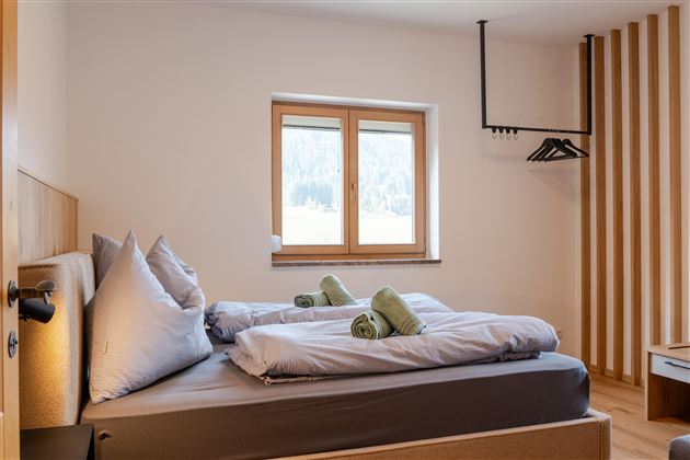 Een heldere slaapkamer met een tweepersoonsbed en twee groene handdoeken. Door het raam valt daglicht op de minimalistische inrichting.