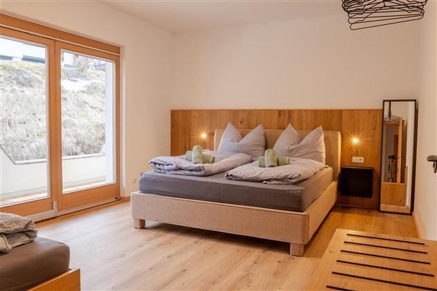 Een moderne slaapkamer met een comfortabel tweepersoonsbed en twee kussens. Grote ramen bieden veel natuurlijk licht en een uitzicht op het landschap.