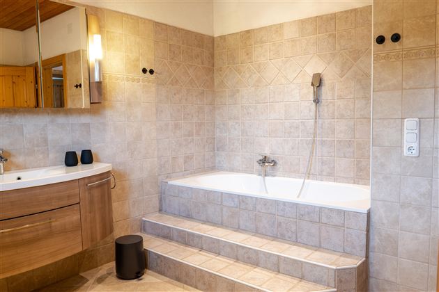 Een moderne badkamer met een bad en een douche. De wanden zijn betegeld in neutrale beige en bruin tinten.