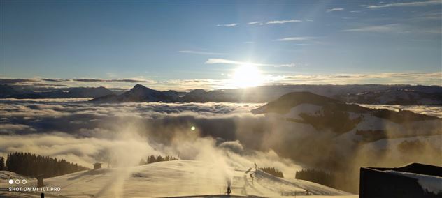 A breathtaking winter landscape with snow-covered mountains and a radiant sun. The sky is clear and the fog envelops the valleys.