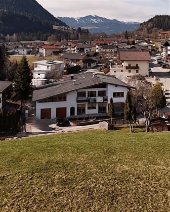A picturesque village with a quiet residential area and mountains in the background. The houses are surrounded by meadows and trees.