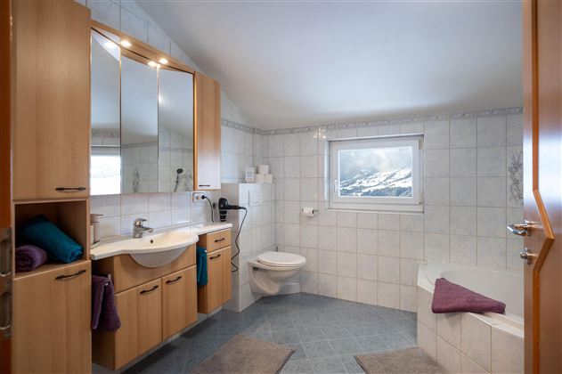 Ein modernes Badezimmer mit hellen Fliesen und Holzschränken. Es verfügt über ein Waschbecken, eine Toilette und eine Badewanne.