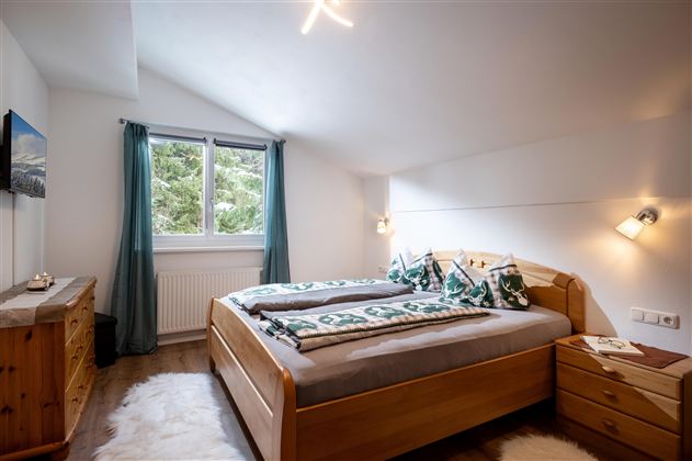 Ein gemütliches Schlafzimmer mit zwei Betten und einem großen Fenster. Die Einrichtung besteht aus Holz und die Wände sind hell gestrichen.