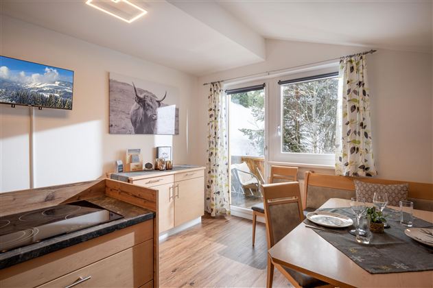 Eine moderne Küche mit einem Esstisch und Stühlen. große Fenster lassen viel Licht herein und bieten einen Blick ins Freie.