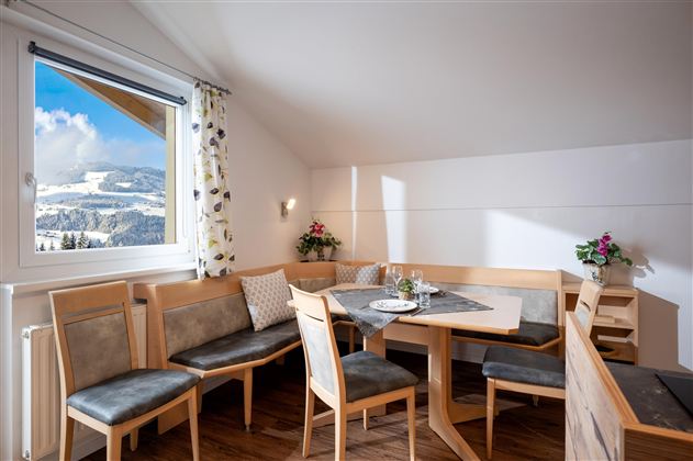 Ein gemütlicher Essbereich mit hellem Holz und modernen Stühlen. Große Fenster bieten einen schönen Ausblick auf die Berge.