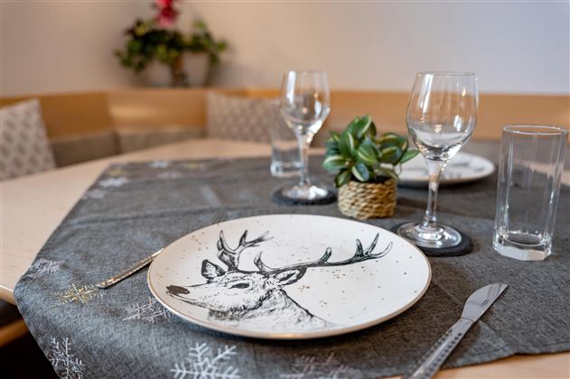 Ein festlich gedeckter Tisch mit einem dekorativen Teller, der ein Reh-Motiv zeigt. Gläser und eine kleine Pflanze ergänzen die Tischdekoration.