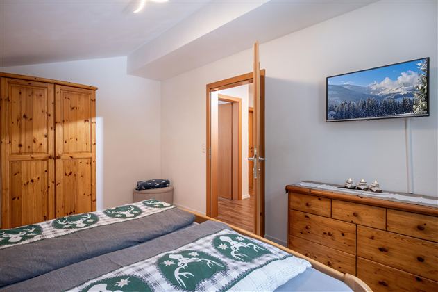 Ein gemütliches Schlafzimmer mit zwei Betten, einem Fernseher und einem Holzschrank. Die Wände sind hell gestrichen, und es gibt eine Tür zu einem anderen Raum.