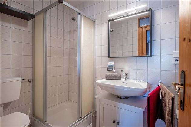 Ein modernes Badezimmer mit Dusche, Waschbecken und Spiegel. Die Wände sind gefliest, und es gibt dekorative Handtücher in verschiedenen Farben.