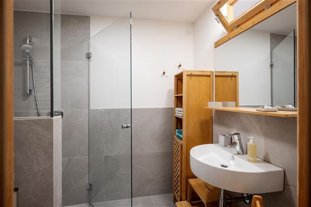 Een moderne badkamer met een betegende douche en een wastafel. Houten planken bieden ruimte voor handdoeken en verzorgingsproducten.