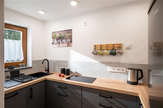 Een moderne keuken met een houten werkblad en zwarte meubels. Een raam laat veel licht binnenkomen en er zijn enkele keukenbenodigdheden aan de muur.