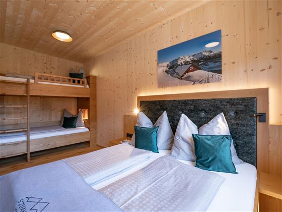 A cozy bedroom with wood paneling and two beds. The walls are decorated with a picture of the mountains.