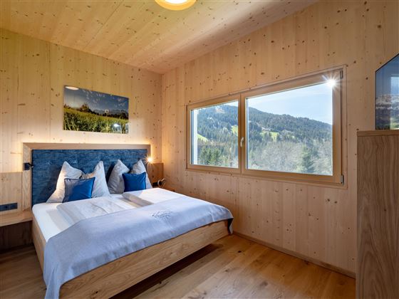 A cozy bedroom with wooden paneling and large windows. You have a beautiful view of the mountains.