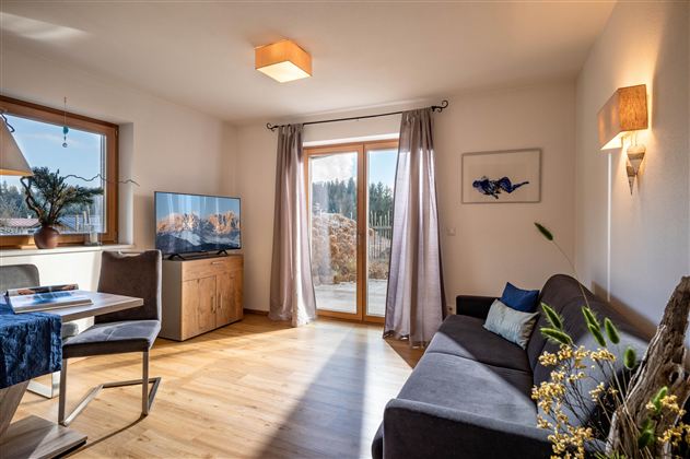 A modern living room with a cozy couch and a table. Large windows let in plenty of light and offer a view of nature.