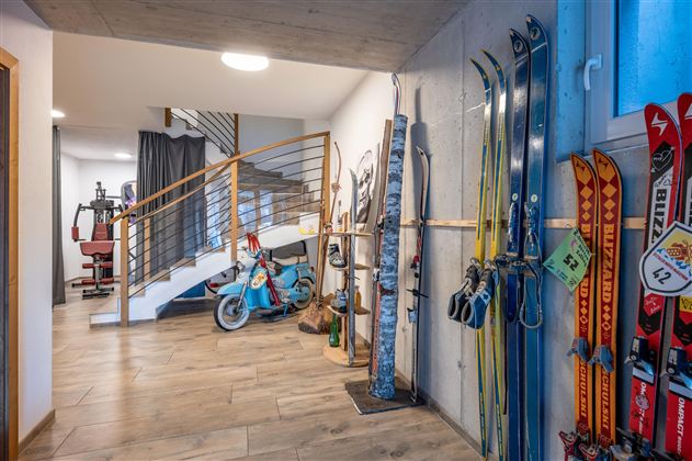 A modern foyer with skis and an old bicycle. The walls are in neutral tones and there is a staircase in the background.