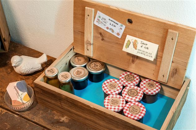 A wooden box with various jars and jam with checkered lids. It also contains small signs with prices.