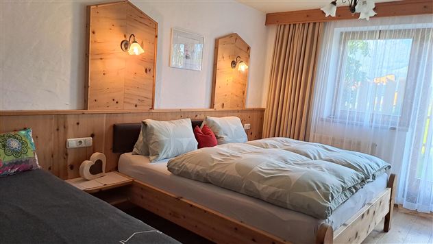 Ein gemütliches Schlafzimmer mit zwei Betten aus Holz. Es gibt sanfte Beleuchtung, helle Vorhänge und ein Fenster, das Tageslicht hereinschickt.