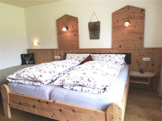 Ein gemütliches Schlafzimmer mit einem Holzbett und schöner Bettwäsche. Die Wände sind aus Holz, und es gibt sanftes Licht von den Wandlampen.