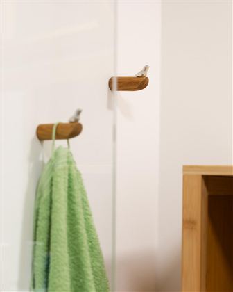 Een minimalistisch badkamergebied met een groene handdoek die aan een houten houder hangt. Op de achtergrond is een glazen wand en een wandplank zichtbaar.