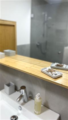 Een modern badkamer met een houten plank en een wastafel. Op de achtergrond is een inloopdouche te zien.