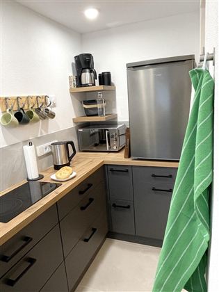 Een moderne keuken met een houten werkblad, een koelkast en een magnetron. Keukenbenodigdheden en kopjes hangen netjes aan de muur.