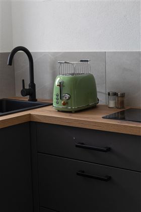 Een moderne toaster in een minimalistische keukenomgeving. De combinatie van een groene toaster, een houten werkblad en donkere kasten creëert een uitnodigende sfeer.