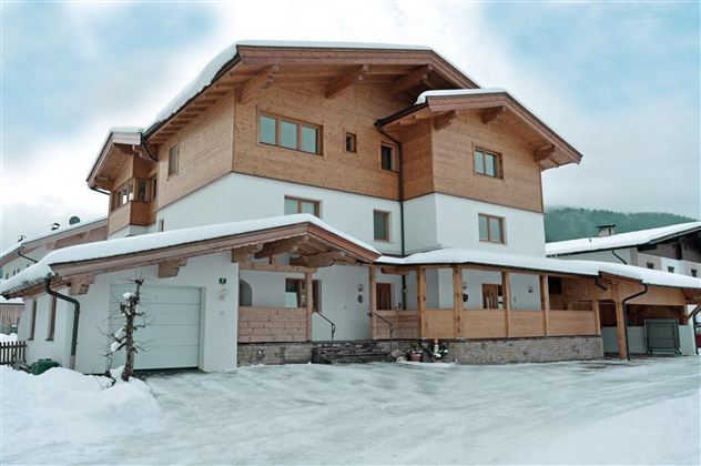Ein modernes Holzhaus im Schnee, umgeben von einer winterlichen Landschaft. Der Himmel ist bewölkt und die Architektur ist gemütlich und einladend.