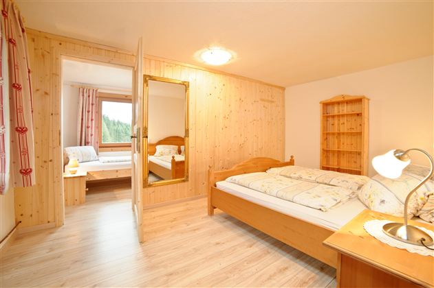 Ein einfaches Schlafzimmer mit Holzverkleidungen und einem großen Fenster. Es gibt zwei Betten, einen Nachttisch und einen Schrank.