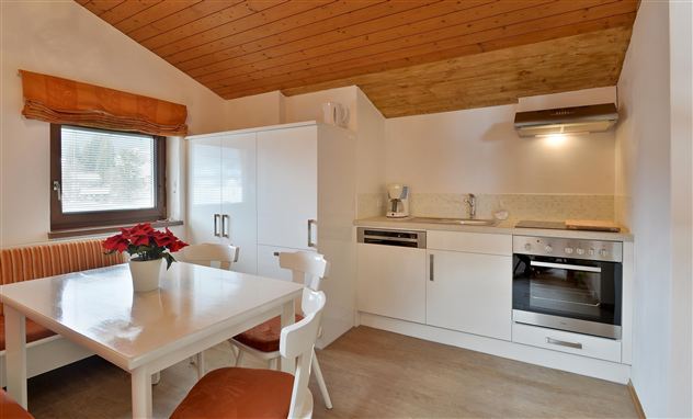 Eine moderne Küche mit einem Esstisch und weißen Möbeln. Der Boden ist hell, und das Holzdecke sorgt für eine warme Atmosphäre.