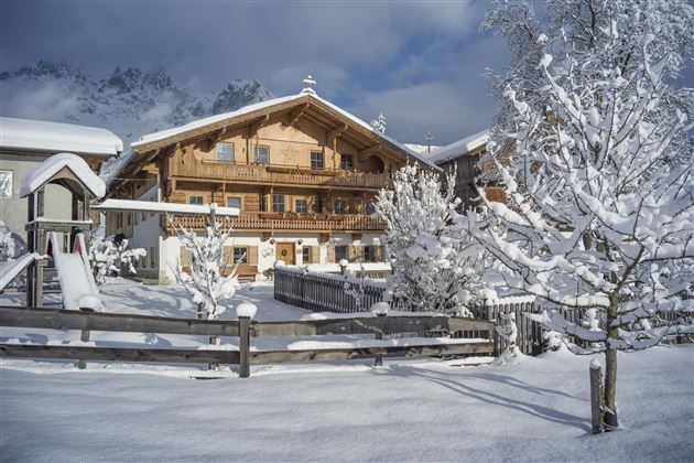 A cozy wooden house in the snow, surrounded by snow-covered trees. The sky is clear and the landscape looks peaceful.