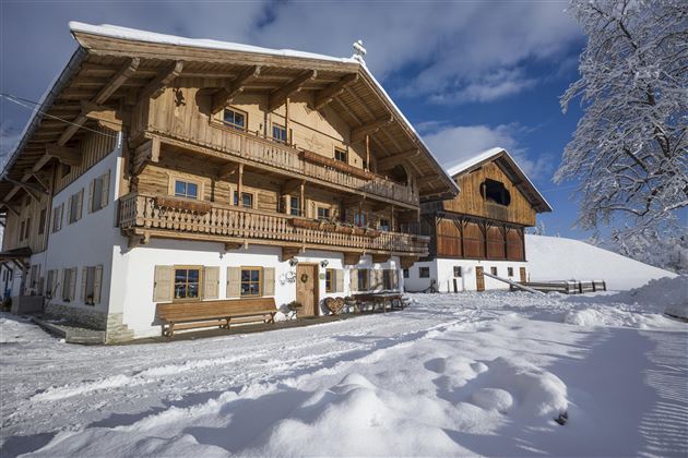 A traditional wooden house in a snowy landscape. The sky is clear and blue, and the surroundings are calm and wintry.