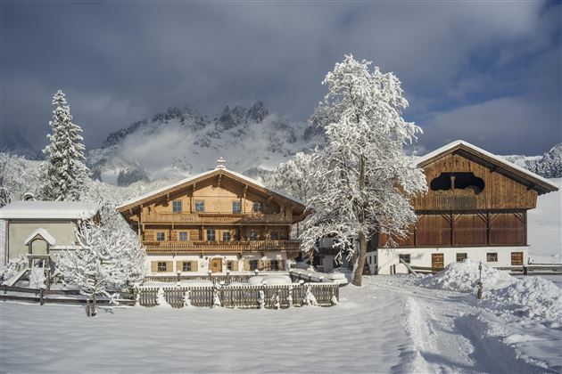 A picturesque winter landscape with snow-covered cottages and trees. In the background, majestic mountains rise under a clear sky.