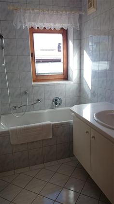 A bright bathroom with a bathtub, a sink, and a window. The tiles are in light colors and create a friendly atmosphere.